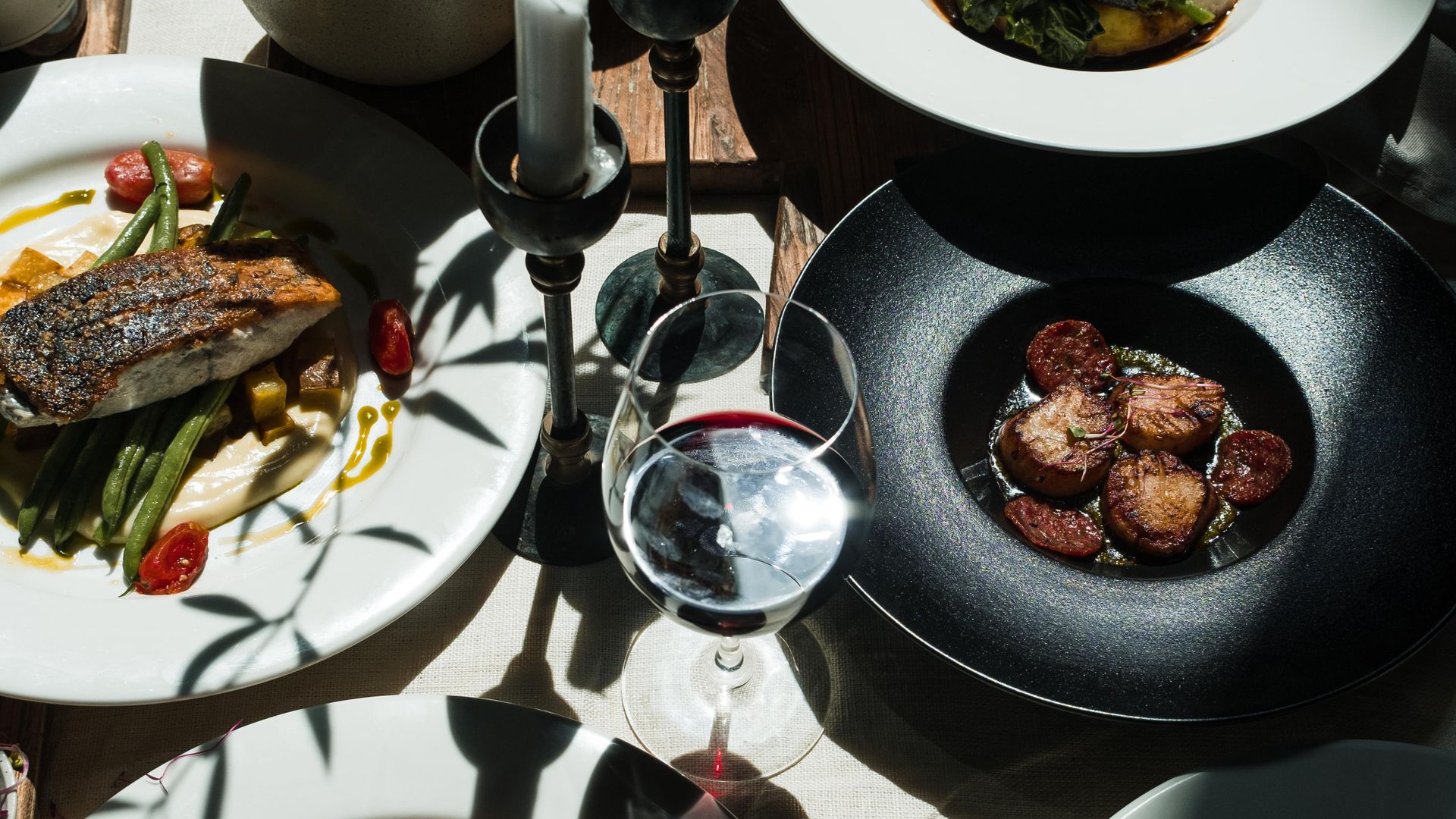 Mesa de restaurante con platos gourmet, velas y vino en luz cálida